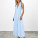 A woman modeling a light blue halter-neck maxi dress with a deep V-neckline, photographed against a white studio wall and gray floor.