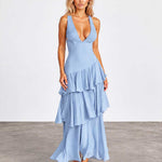 A woman modeling a light blue sleeveless maxi dress with a deep V-neckline and a tiered ruffle skirt, standing against a neutral studio backdrop.
