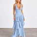 A woman modeling a light blue sleeveless maxi dress with a deep V-neckline and a tiered ruffle skirt, standing against a neutral studio backdrop.