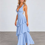 A woman modeling a light blue sleeveless maxi dress with a deep V-neckline, side cutouts, and a tiered ruffled skirt, paired with clear high-heeled sandals against a neutral studio backdrop.