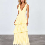 A woman modeling a pale yellow sleeveless maxi dress with a deep V-neckline, fitted bodice, and tiered ruffle skirt, standing against a light gray studio background.