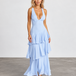A woman modeling a light blue sleeveless maxi dress with a deep V-neckline and a tiered ruffle skirt, standing against a neutral studio backdrop.