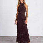 A woman modeling a sleeveless, high-neck, floor-length lace maxi dress in a deep dark brown color, standing against a light gray studio background.
