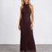 A woman modeling a sleeveless, high-neck, floor-length lace maxi dress in a deep dark brown color, standing against a light gray studio background.