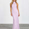 A woman modeling a sleeveless, high-neck, floor-length lavender lace maxi dress against a white studio wall and gray floor.