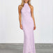 A woman modeling a sleeveless, high-neck, floor-length lavender lace maxi dress against a white studio wall and gray floor.