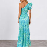 A woman modeling a one-shoulder maxi dress with a vibrant blue and green floral print, shown from the back against a plain studio background.