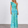 A woman modeling a one-shoulder maxi dress with a vibrant turquoise and teal floral print, standing against a neutral studio background.