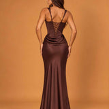 A woman wearing a floor-length satin-like gown shown from the back against a warm tan studio backdrop. The dress is a deep chocolate brown with a lace-up open back and fitted silhouette.