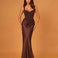 A woman modeling a floor-length, satin-like dark brown gown with a sweetheart neckline, structured bodice, draped waist, and fitted mermaid-style skirt against a warm tan studio backdrop.