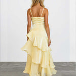 A woman viewed from behind wearing a pale yellow ruffled spaghetti-strap dress with a structured bodice and layered skirt, standing against a plain light gray wall and concrete floor.