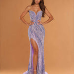 A woman modeling a strapless lavender and silver sequined floor-length gown with a sweetheart neckline, thigh-high slit, and slight train against a warm tan studio backdrop.