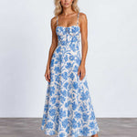 A woman modeling a sleeveless midi dress with thin straps, a gathered sweetheart neckline, and a blue floral toile pattern on a white background, standing against a light gray studio backdrop.