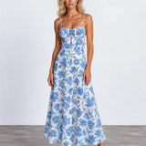 A woman modeling a sleeveless midi dress with thin straps, a gathered sweetheart neckline, and a blue floral toile pattern on a white background, standing against a light gray studio backdrop.