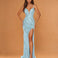 A woman modeling a floor-length light blue evening gown with thin straps, a deep V-neckline, a high thigh slit, and an embellished draped bodice, posed against a warm tan studio backdrop.