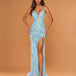A woman modeling a floor-length light blue evening gown with thin straps, a deep V-neckline, a high thigh slit, and an embellished draped bodice, posed against a warm tan studio backdrop.