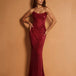A woman modeling a strapless, floor-length mermaid gown covered in shimmering red sequins, posed against a solid warm tan studio backdrop.