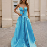 Woman wearing a blue formal strapless gown standing on a stone pavement.