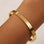 Gold bracelet with diamond accents on a wrist against a beige background