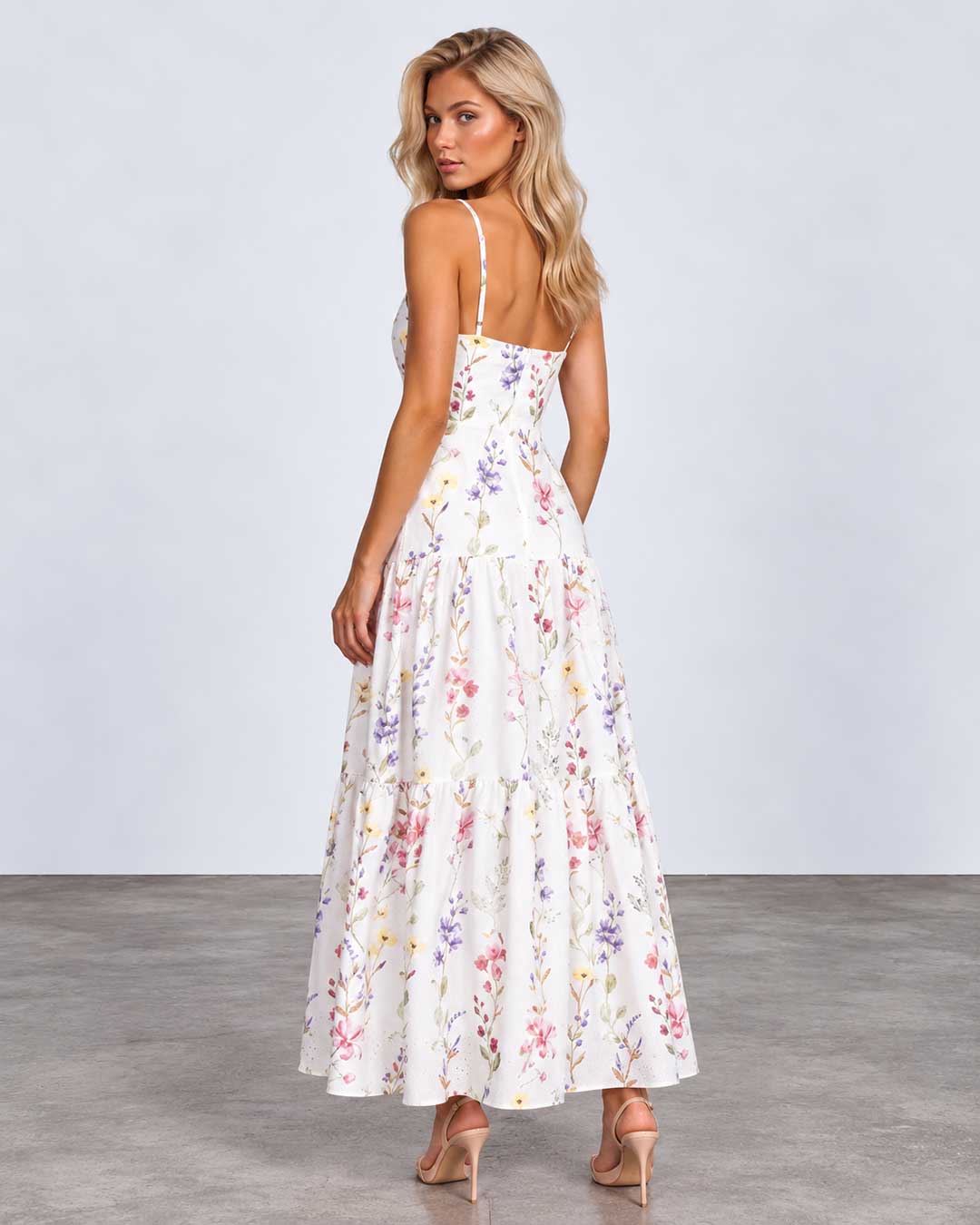 A woman modeling a white maxi dress with a colorful pastel floral print, shown from the back against a light gray studio background.