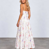 A woman modeling a white maxi dress with a colorful pastel floral print, shown from the back against a light gray studio background.