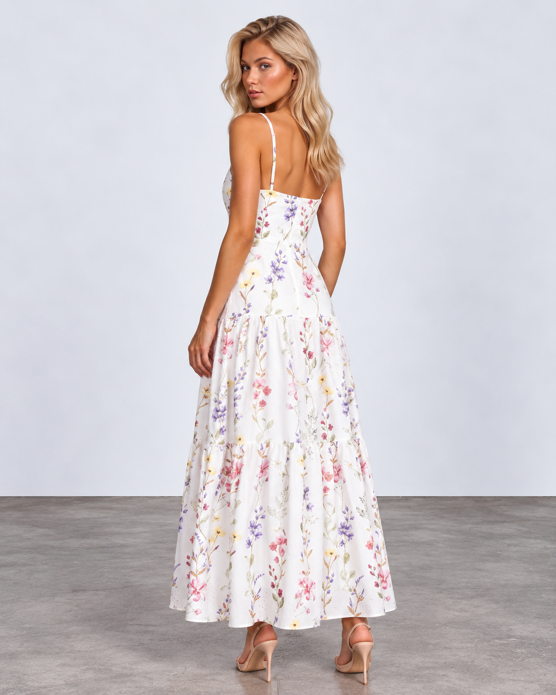A woman modeling a white spaghetti-strap maxi dress with a colorful pastel floral print, shown from the back against a light gray studio background.