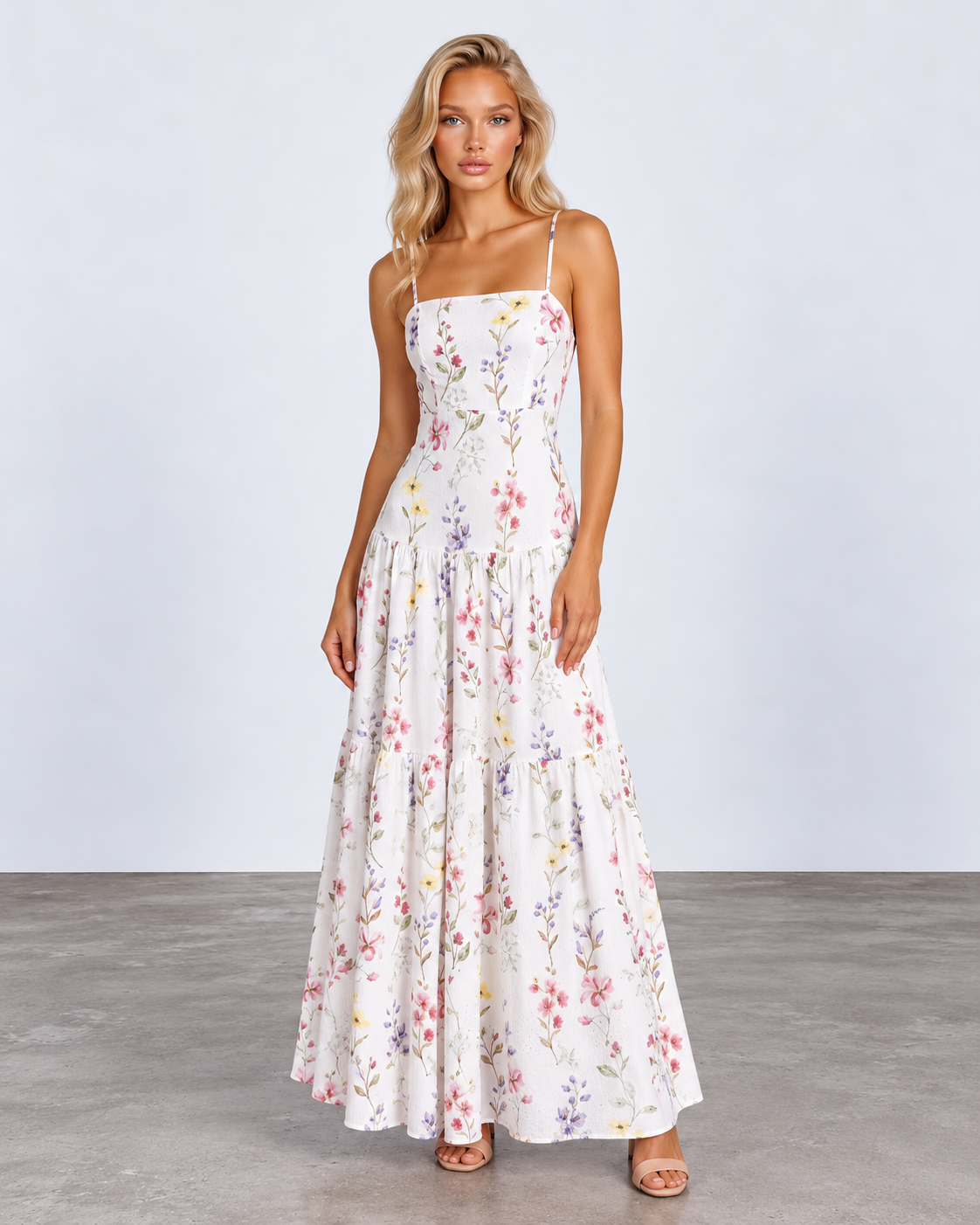 A woman modeling a white spaghetti-strap maxi dress with a colorful pastel floral print, standing against a light gray studio background.