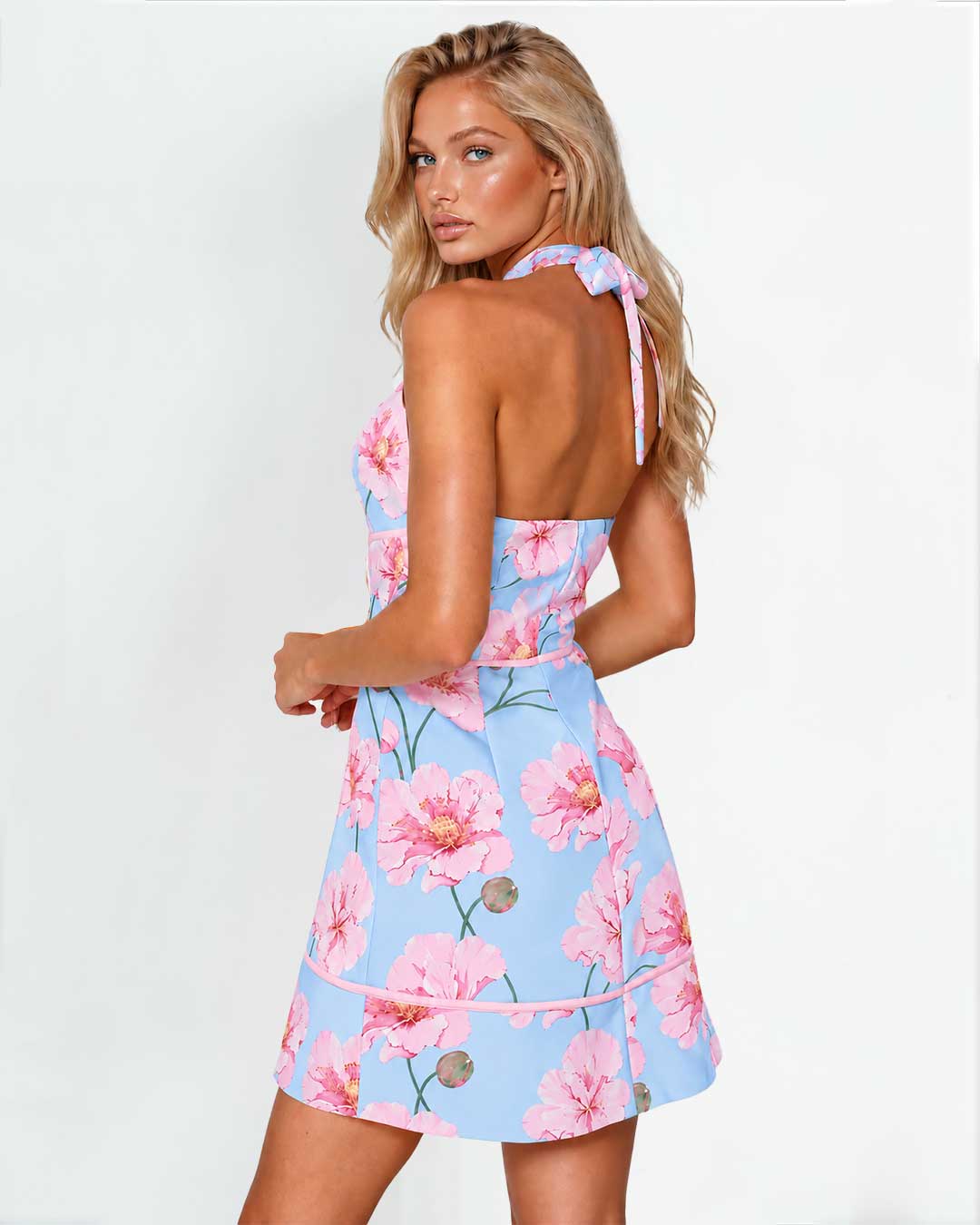 A woman modeling a light blue halter mini dress with a pink floral print, shown from the back against a plain white studio background.
