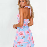 A woman modeling a light blue halter mini dress with a pink floral print, shown from the back against a plain white studio background.