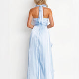 A woman shown from the back wearing a light blue halter-neck maxi dress with a tied back and flowing skirt, photographed against a plain white studio background.