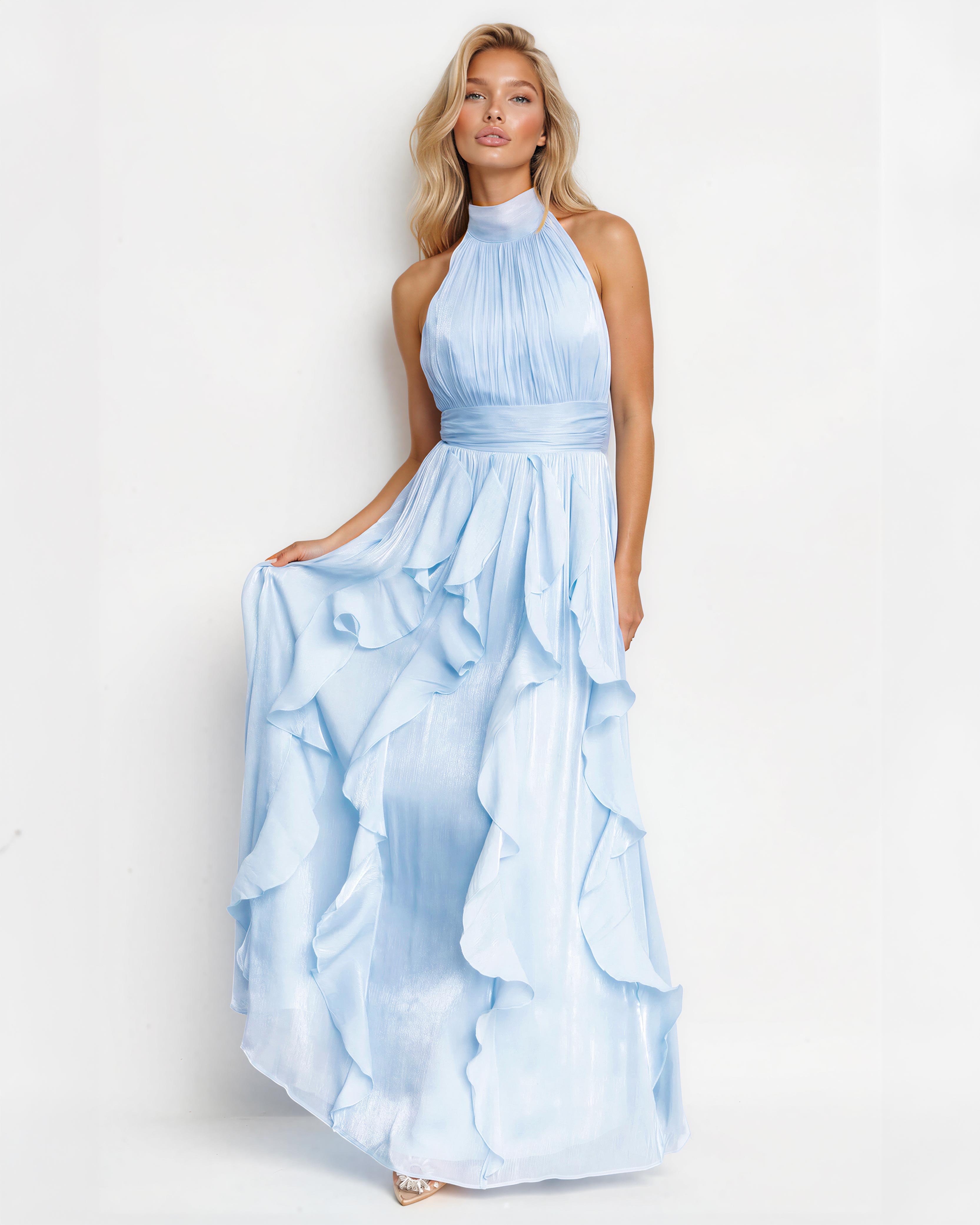 A blonde model wearing a light blue halter-neck maxi dress with a pleated bodice and a layered ruffled skirt, standing against a plain white studio background.