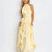 A woman modeling a pale yellow halter-neck maxi dress with a gathered waist and layered ruffle skirt, photographed against a plain white studio background.