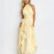 A woman modeling a pale yellow halter-neck maxi dress with a gathered waist and layered ruffle skirt, photographed against a plain white studio background.