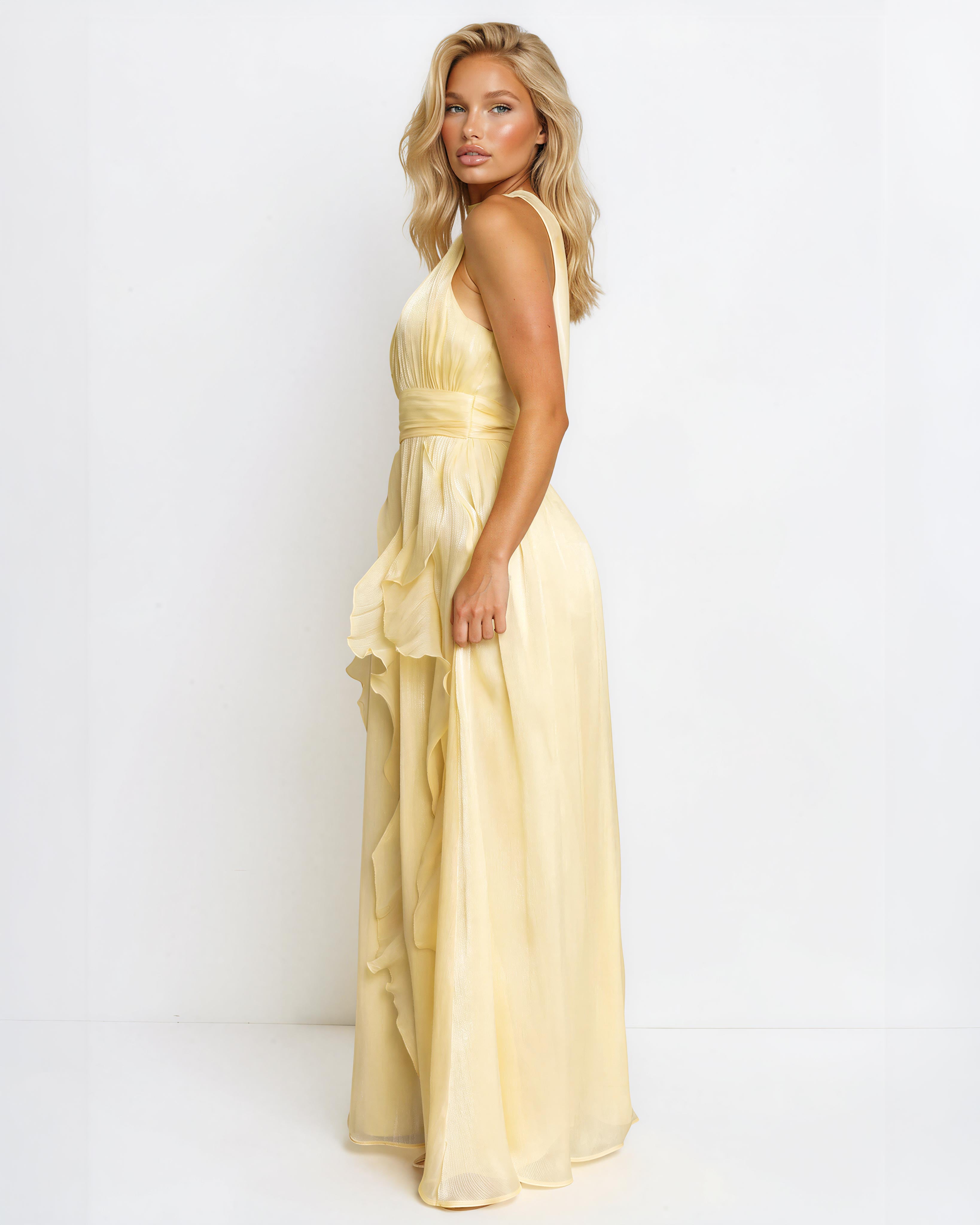A blonde model wearing a pale yellow sleeveless maxi dress with a ruffled hem, photographed against a plain white studio background.