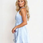 A blonde model wearing a light blue halter-neck mini dress, shown from a side-back angle against a plain white studio background.