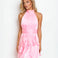 A blonde model wearing a light pink halter-neck mini dress with a ruffled tiered skirt, posed against a plain white studio background.
