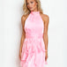 A blonde model wearing a light pink halter-neck mini dress with a ruffled tiered skirt, posed against a plain white studio background.