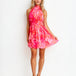 A woman modeling a sleeveless halter-neck mini dress with a vibrant pink and orange tie-dye pattern, standing against a plain white studio background.