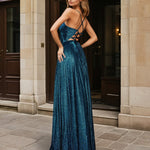 Woman in a teal evening glitter formal dress gown with a high slit standing outdoors.