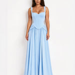 A woman modeling a light blue sleeveless maxi dress with a fitted corset-style bodice and a flowing skirt, standing against a plain white studio background.