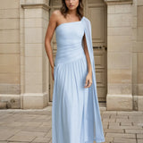 Woman wearing a light blue one-shoulder dress standing in front of a stone building.