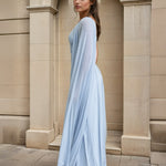 Woman wearing a light blue one-shoulder dress standing in front of a stone building.