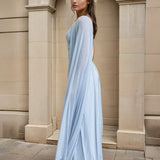 Woman wearing a light blue one-shoulder dress standing in front of a stone building.