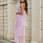 Woman wearing a light purple dress standing against a stone building.