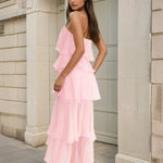 Woman wearing a pink ruffled dress standing against a stone building.