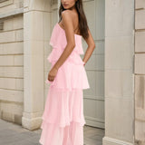 Woman wearing a pink ruffled dress standing against a stone building.