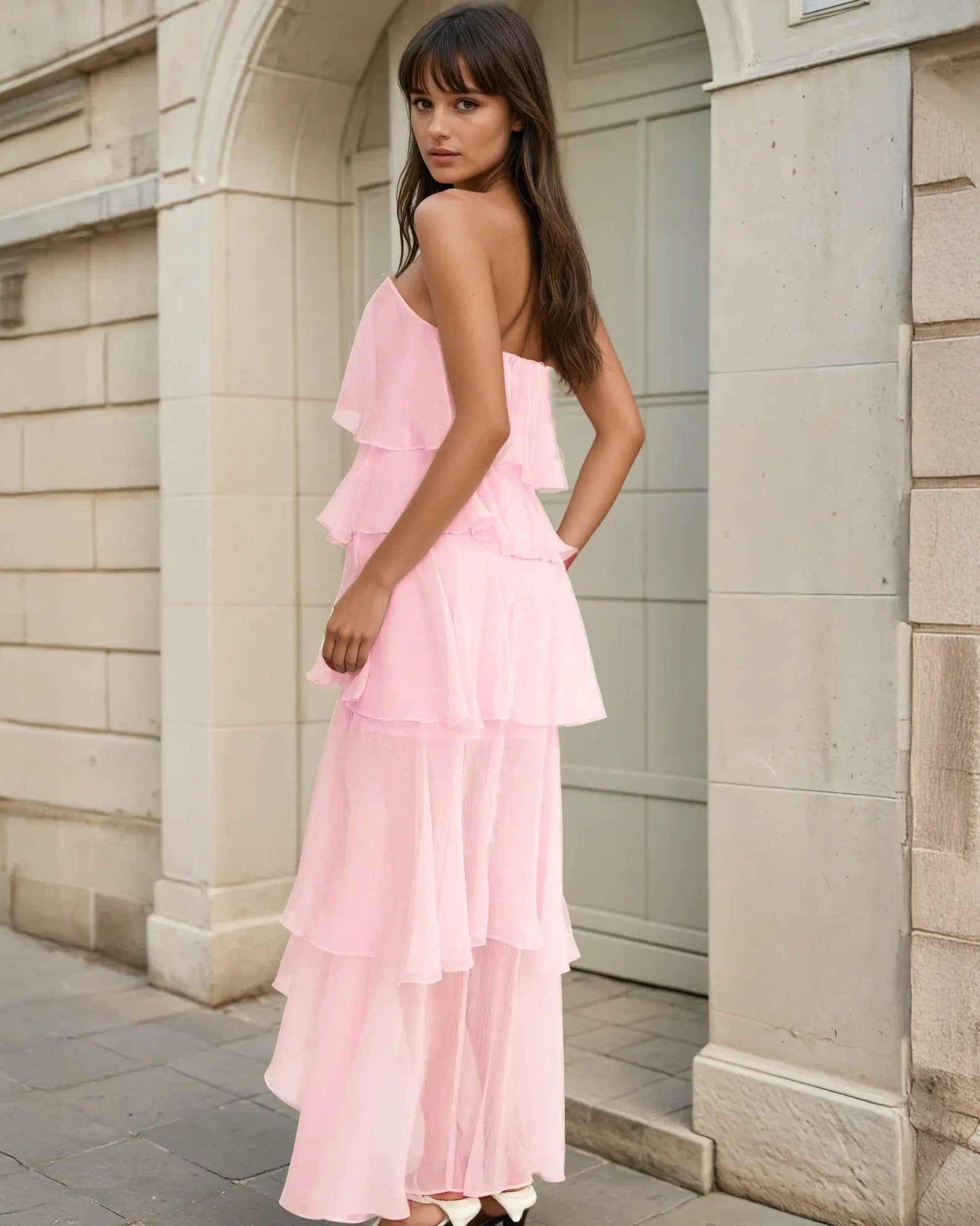 Woman wearing a pink ruffled dress standing against a stone building.