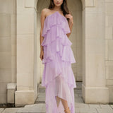 Woman wearing a purple ruffled dress standing in front of a stone archway.