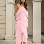 Woman wearing a pink ruffled dress standing in front of a stone archway.