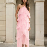 Woman wearing a pink ruffled dress standing in front of a stone archway.